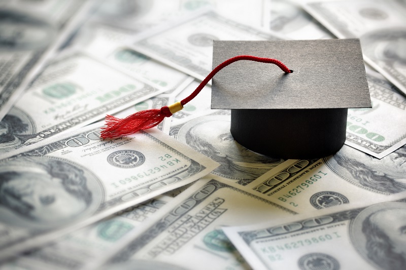 Graduation cap on top of many 100-dollar bills.